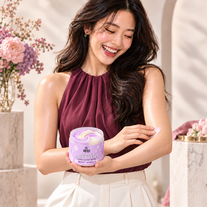 An adult woman applying Body Bliss Berry Vanilla whipped body butter to her arm while holding the lavender-labelled jar.