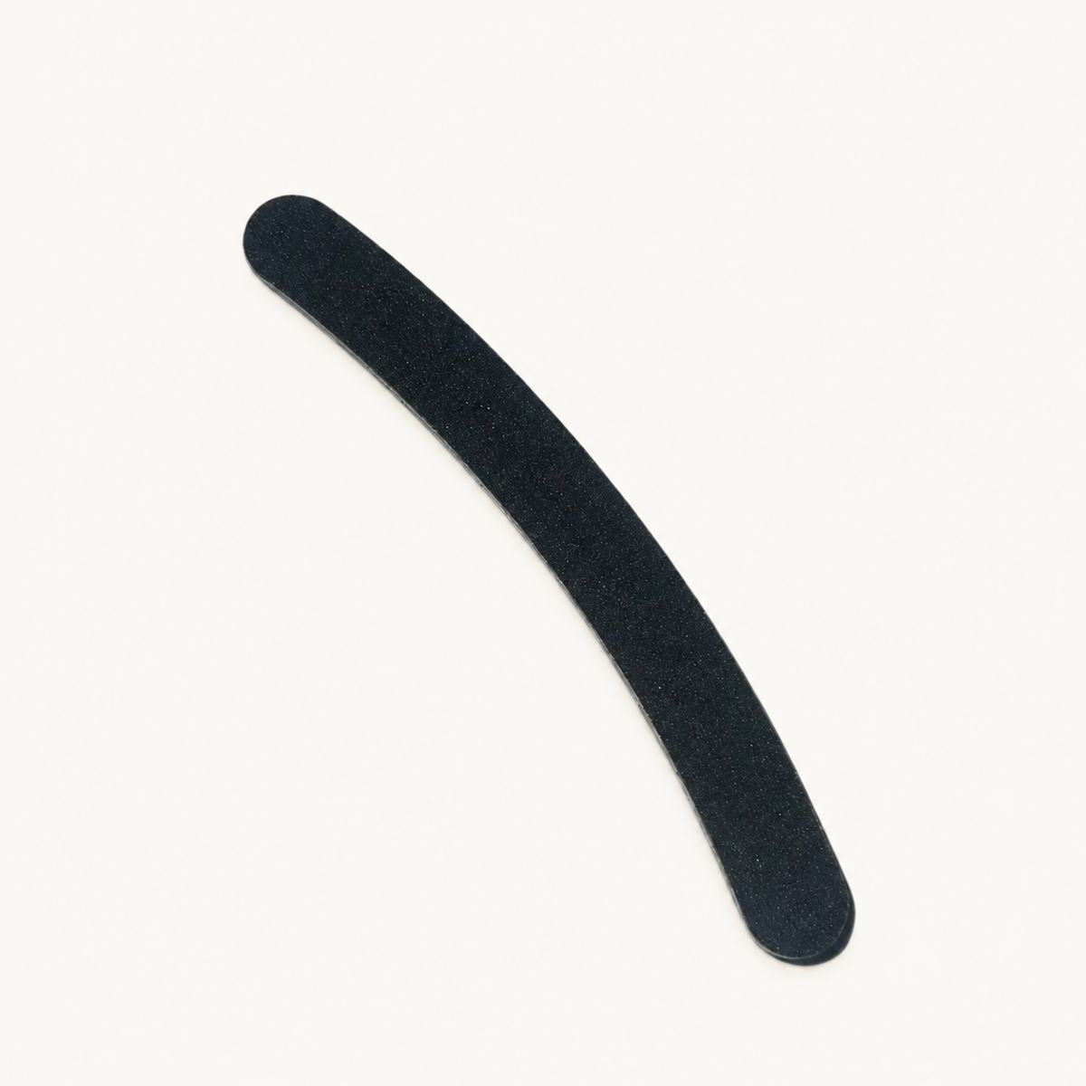 Single curved black Body Bliss banana nail file on a warm ivory background