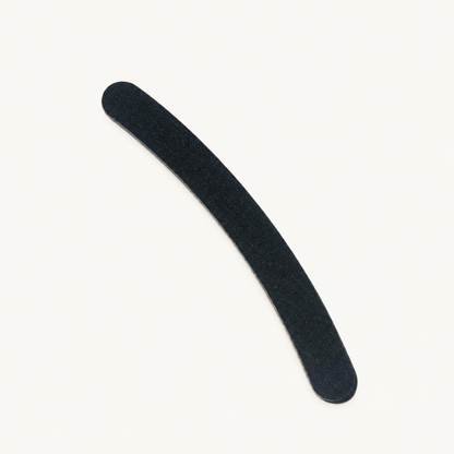 Single curved black Body Bliss banana nail file on a warm ivory background