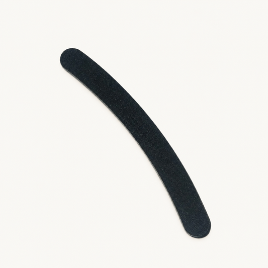 Single curved black Body Bliss banana nail file on a warm ivory background