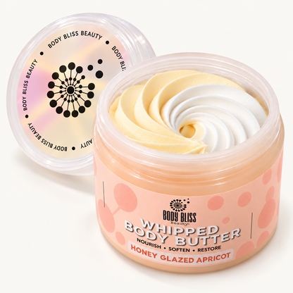 Body Bliss Honey Glazed Apricot whipped body butter in a clear jar with a peach label and pale-yellow and white swirls, on a plain warm ivory background.