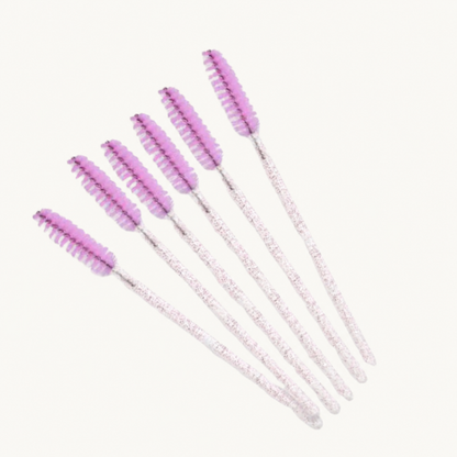 Six pink-lilac eyelash and brow brush wands displayed on a warm ivory background