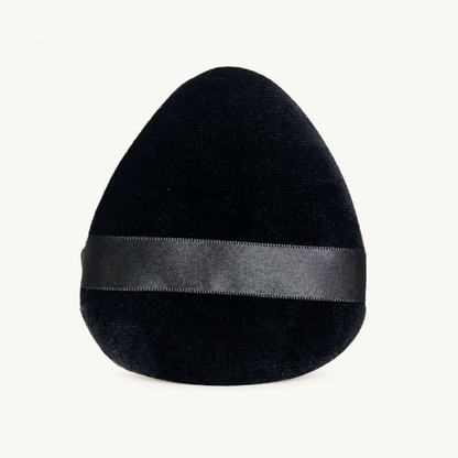 Single black Body Bliss Miracle Blending Facial Makeup Sponge with a horizontal ribbon on a warm ivory background