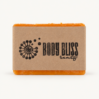 Single orange Body Bliss turmeric kojic soap bar in clear wrapping and a kraft-paper sleeve on warm ivory
